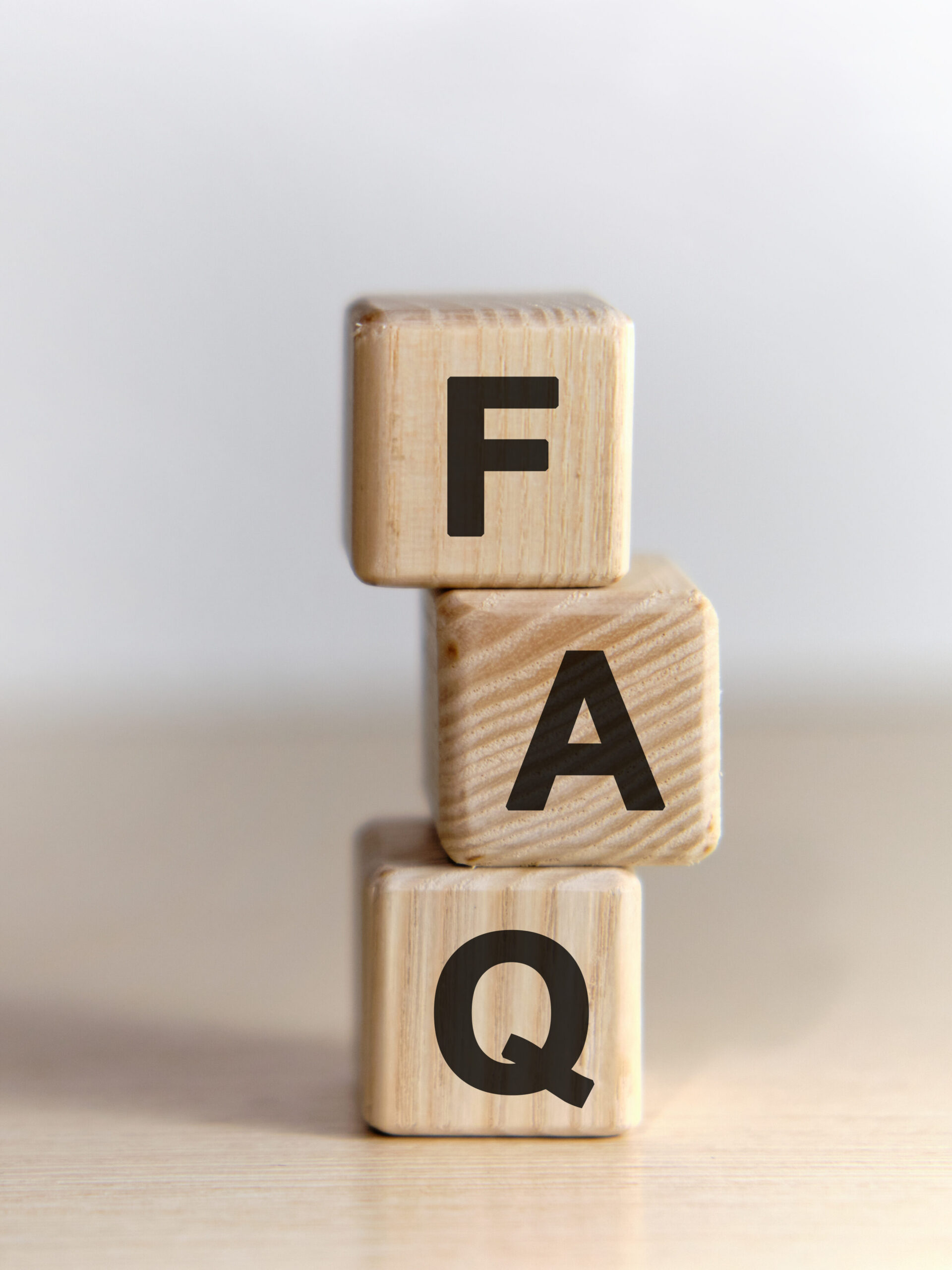 Three wooden blocks stacked vertically, each displaying a black letter. From top to bottom, the blocks read "F," "A," and "Q," representing the acronym for Frequently Asked Questions. The background is plain and light.