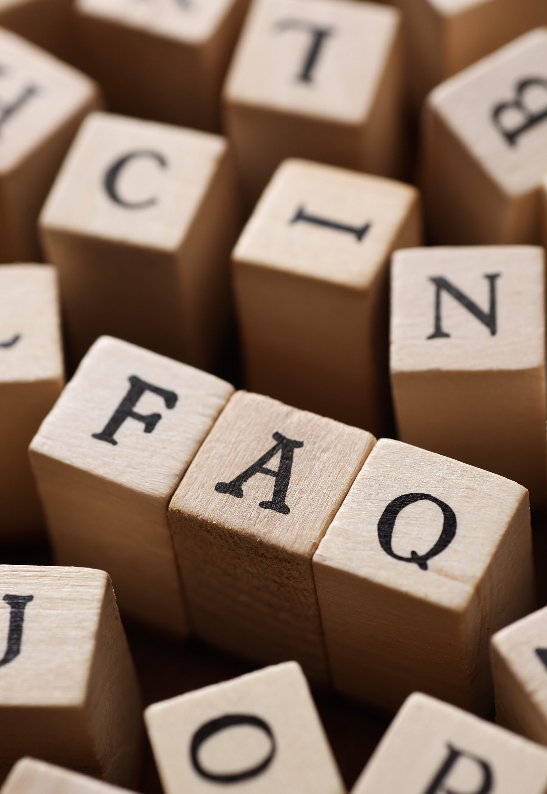 Close-up of wooden blocks with letters, with three blocks in the center spelling out "FAQ". Other blocks with various letters are blurred in the background.
